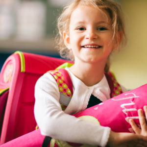 Ein Mädchen mit Schulranzen hält eine rosa Schultüte im Arm 