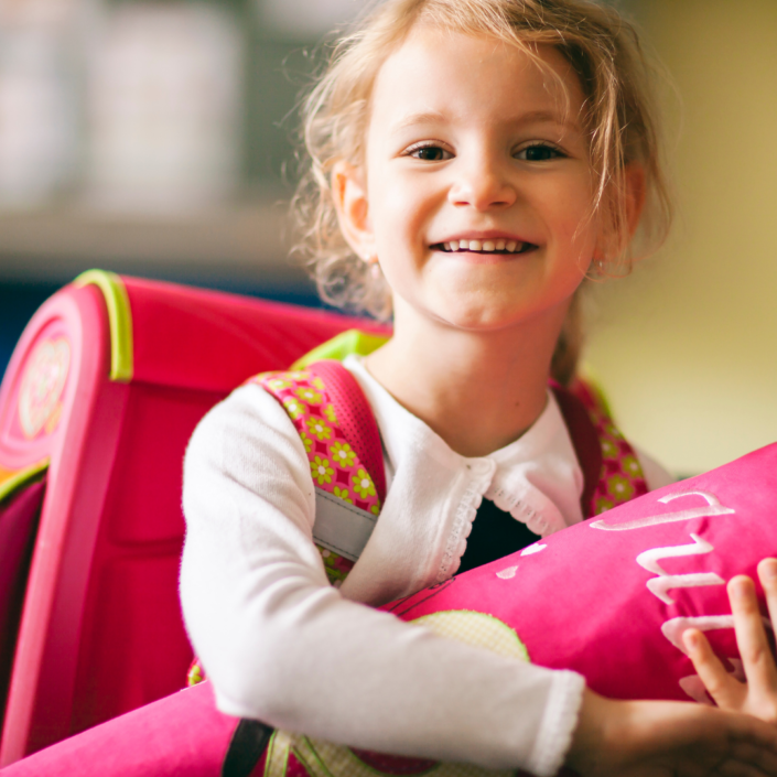 Schultüte Ein Mädchen mit Schulranzen hält eine rosa Schultüte im Arm